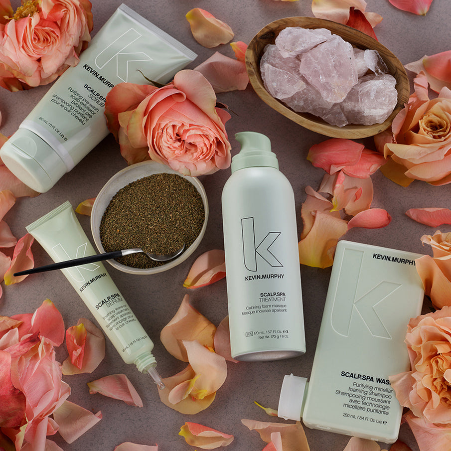 Kevin Murphy hair care products surrounded by flowers and rose petals on a textured surface.